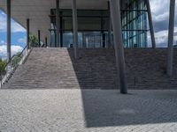 a person on a bike walking through a stone building entrance, in front of an enormous glass wall and stairs