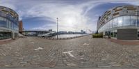 a 360 - effect photograph of two circular buildings at waterfront park with boats parked in background