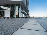 a sidewalk leading into an empty area next to a river and tall buildings near the water