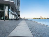 a sidewalk leading into an empty area next to a river and tall buildings near the water