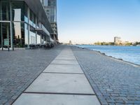 a sidewalk leading into an empty area next to a river and tall buildings near the water