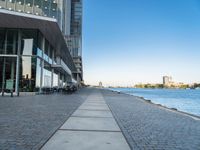 a sidewalk leading into an empty area next to a river and tall buildings near the water