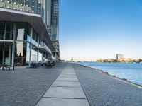 a sidewalk leading into an empty area next to a river and tall buildings near the water