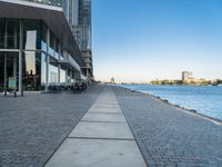 a sidewalk leading into an empty area next to a river and tall buildings near the water