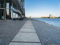 a sidewalk leading into an empty area next to a river and tall buildings near the water