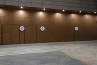 an empty brown tiled floor with doors and lights above it that include four round clocks