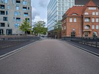 an empty street is shown with some buildings in the background while the pedestrian bridge leads down