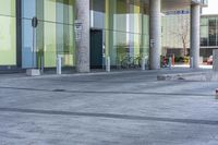 an empty plaza with benches and steps leading into a building with columns, green walls, and a bike parked in the background