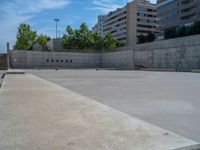 the empty parking lot in front of a wall with apartment buildings on it and a skateboarder on a ramp