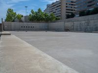 the empty parking lot in front of a wall with apartment buildings on it and a skateboarder on a ramp