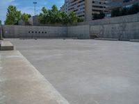 the empty parking lot in front of a wall with apartment buildings on it and a skateboarder on a ramp