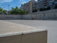 the empty parking lot in front of a wall with apartment buildings on it and a skateboarder on a ramp