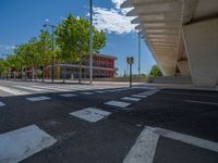 a car sitting at an empty street underneath a overpass overhang that contains a train stop, and cars and a pedestrian