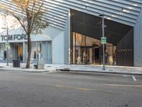 the entrance of a store that is located on the sidewalk in front of a tree