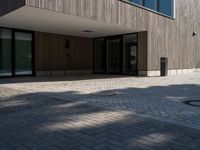 a building is shown with the entrance door open on the cobblestone path, with a trashcan on the sidewalk in front of it