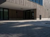 a building is shown with the entrance door open on the cobblestone path, with a trashcan on the sidewalk in front of it