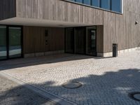 a building is shown with the entrance door open on the cobblestone path, with a trashcan on the sidewalk in front of it