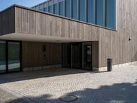 a building is shown with the entrance door open on the cobblestone path, with a trashcan on the sidewalk in front of it