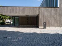 a stone patio with a bench outside of a large wooden building with windows that open onto a paved courtyard