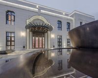 a modern building that is reflected in the water of a reflecting pool with large metal sculpture