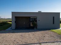 a very neat home with some doors and gravel and plants in front of it in a sunny day