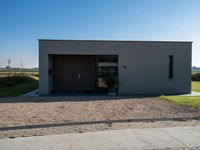 a very neat home with some doors and gravel and plants in front of it in a sunny day