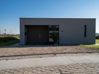 a very neat home with some doors and gravel and plants in front of it in a sunny day