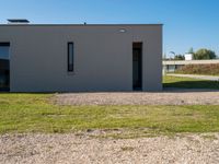 a cement house with small white doors on it's side, with grass and a paved walkway and a dirt path in front of it