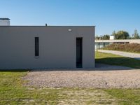 a cement house with small white doors on it's side, with grass and a paved walkway and a dirt path in front of it