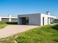 a house sits alone on grass next to a gravel path and a pathway leading through it