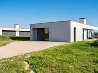 a house sits alone on grass next to a gravel path and a pathway leading through it