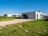 a house sits alone on grass next to a gravel path and a pathway leading through it