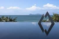 a pool with a triangle reflection in it with a body of water behind it near the ocean