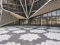 a walkway that has white geometric tiles on it in front of buildings with glass walls