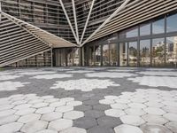 a walkway that has white geometric tiles on it in front of buildings with glass walls