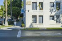 a white apartment building next to the street with cars parked in front of it on the corner