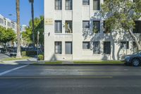 a white apartment building next to the street with cars parked in front of it on the corner