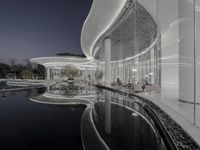 the pool and spa features curved walls and glass windows at night in a modern white building