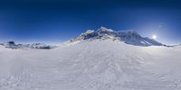 a snow covered mountain with a big sun in the background and a clear sky above it