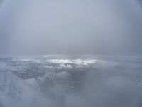 view from an airplane flying over a snowy mountains range in the foggy sky of the ocean