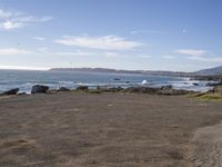 a beach area with rocks and the ocean in the distance and a bird flying overhead