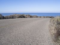 a man riding a skateboard on top of a gravel road next to the ocean