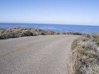 a man riding a skateboard on top of a gravel road next to the ocean