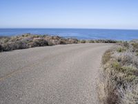 a man riding a skateboard on top of a gravel road next to the ocean