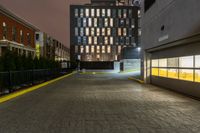 an empty walkway with yellow line dividing it and buildings in the background at night in front of a metal gate