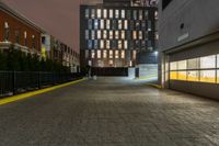 an empty walkway with yellow line dividing it and buildings in the background at night in front of a metal gate