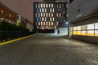 an empty walkway with yellow line dividing it and buildings in the background at night in front of a metal gate