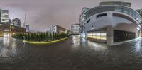 a panoramic shot of a public area with buildings and a clock tower at night