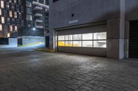 empty parking garage doors at night with yellow light in foreground and grey concrete facade with brick pattern