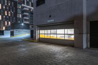 empty parking garage doors at night with yellow light in foreground and grey concrete facade with brick pattern